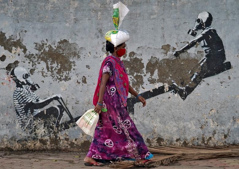 A woman wearing a protective face mask walks past a graffiti, after authorities eased lockdown restrictions that were imposed to slow the spread of the coronavirus disease (COVID-19), in Mumbai, India. REUTERS/Hemanshi Kamani  